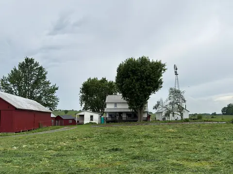 A farmhouse, a red barn and a windmill on a green lawn
