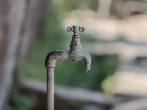 A weathered tap on a pipe in a green yard