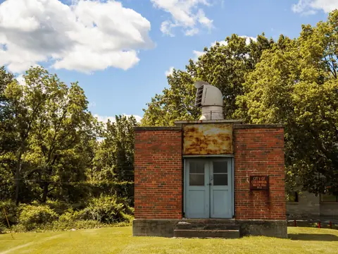 A small brick pump house in a sunny yard among trees
