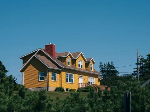 A yellow country house among tall trees under a blue sky
