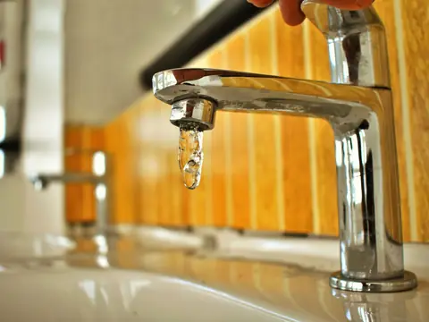 A chrome tap with a single drop of water at the spout